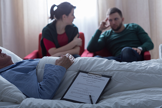 Man and woman discussing in front of a patient with a will in a hospital room