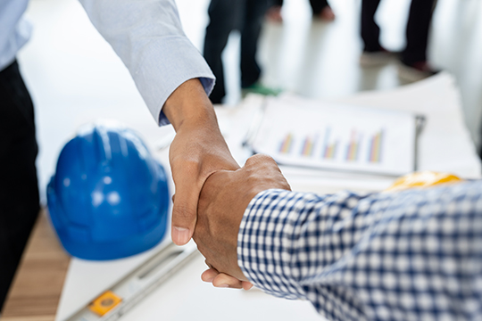 Persons shake hands over building plans